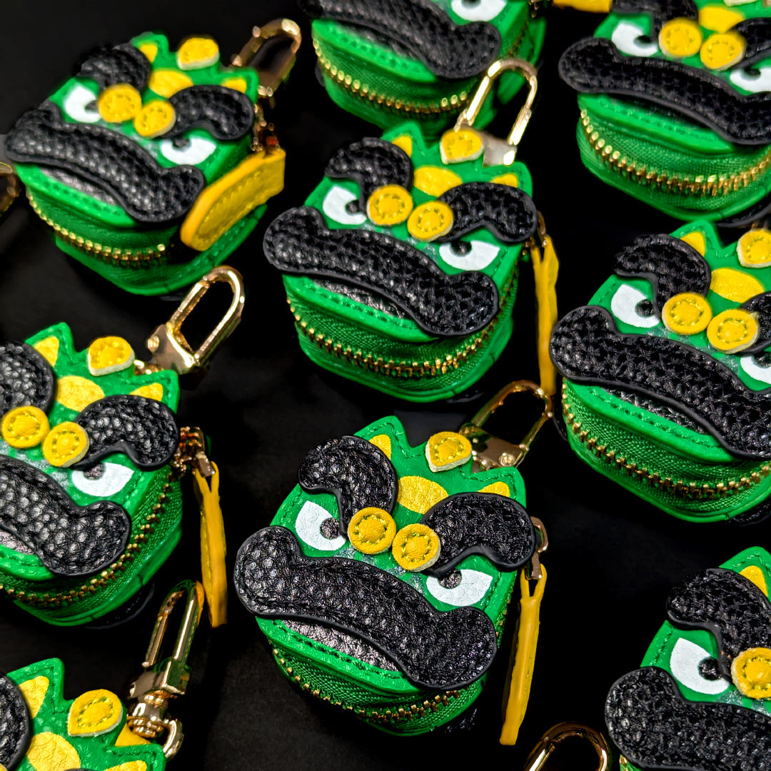 Green and black lion dance head keychains made from vegan leather with yellow accents on a black background
