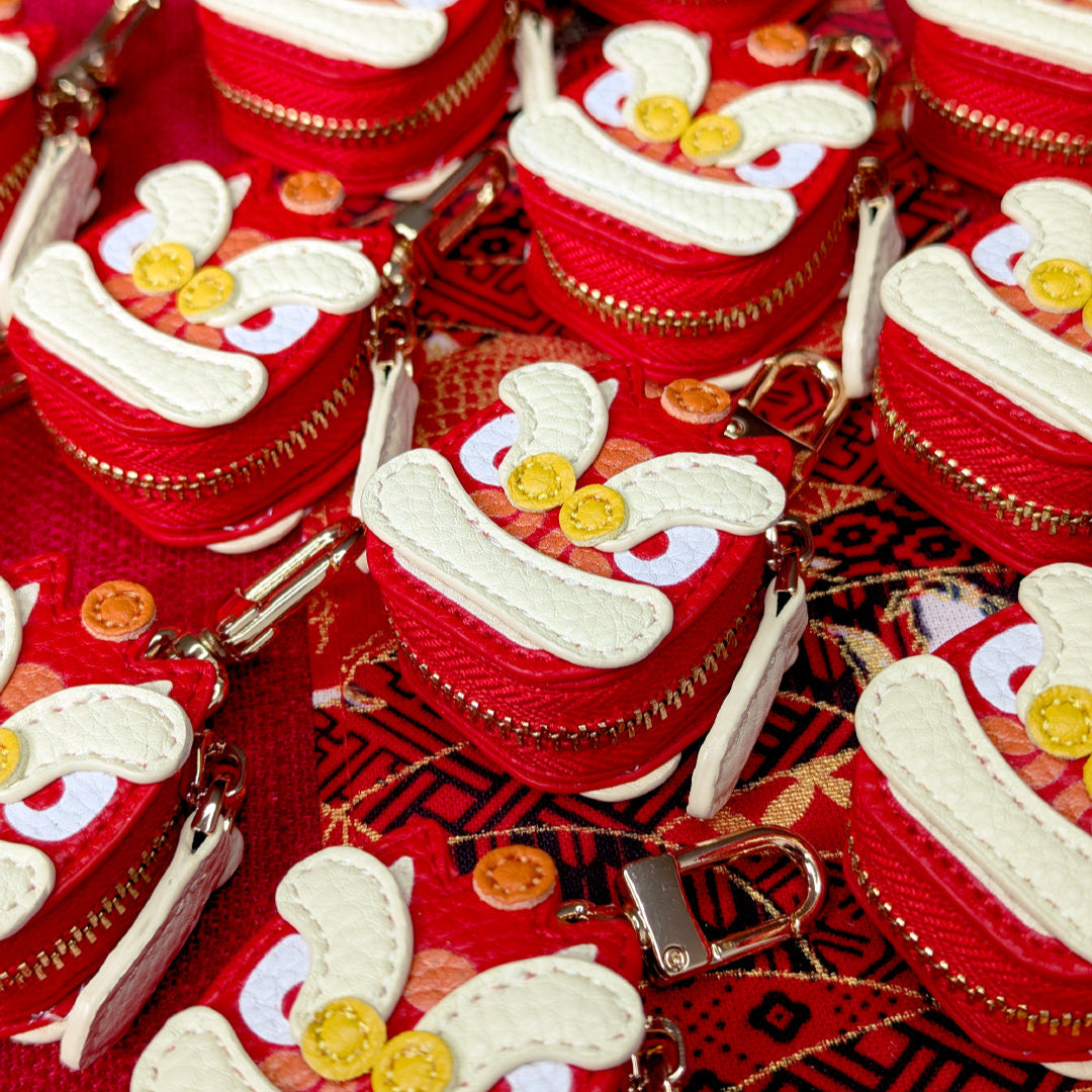 Red and white keychains with lion dance head designs on a red fabric background