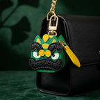 Keychain shaped like a chinese lion dance character with green, yellow, and black colors on a black surface.